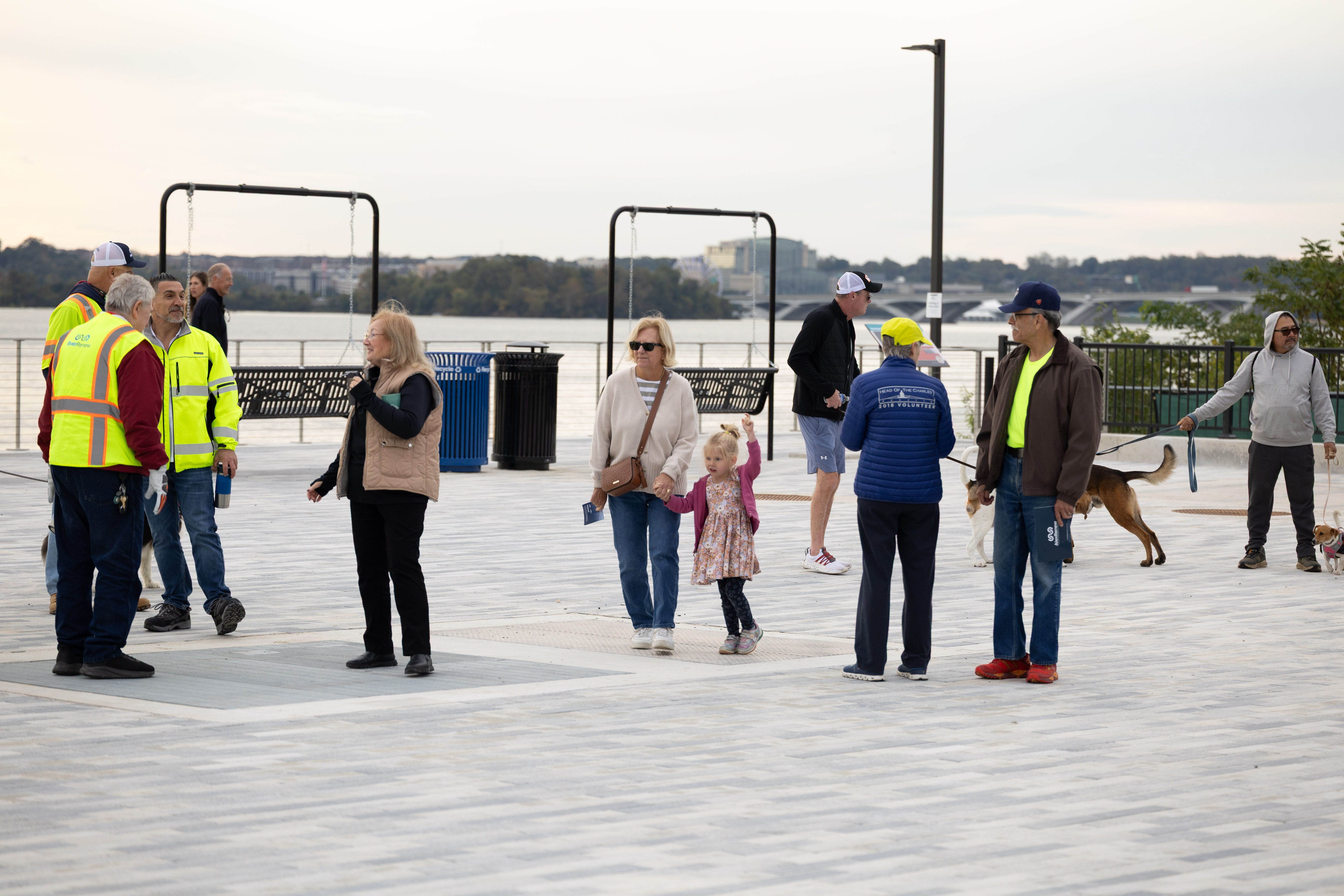People in casual clothing talk to AlexRenew staff in high vis vests. The promenade with a view of the river is in the background.