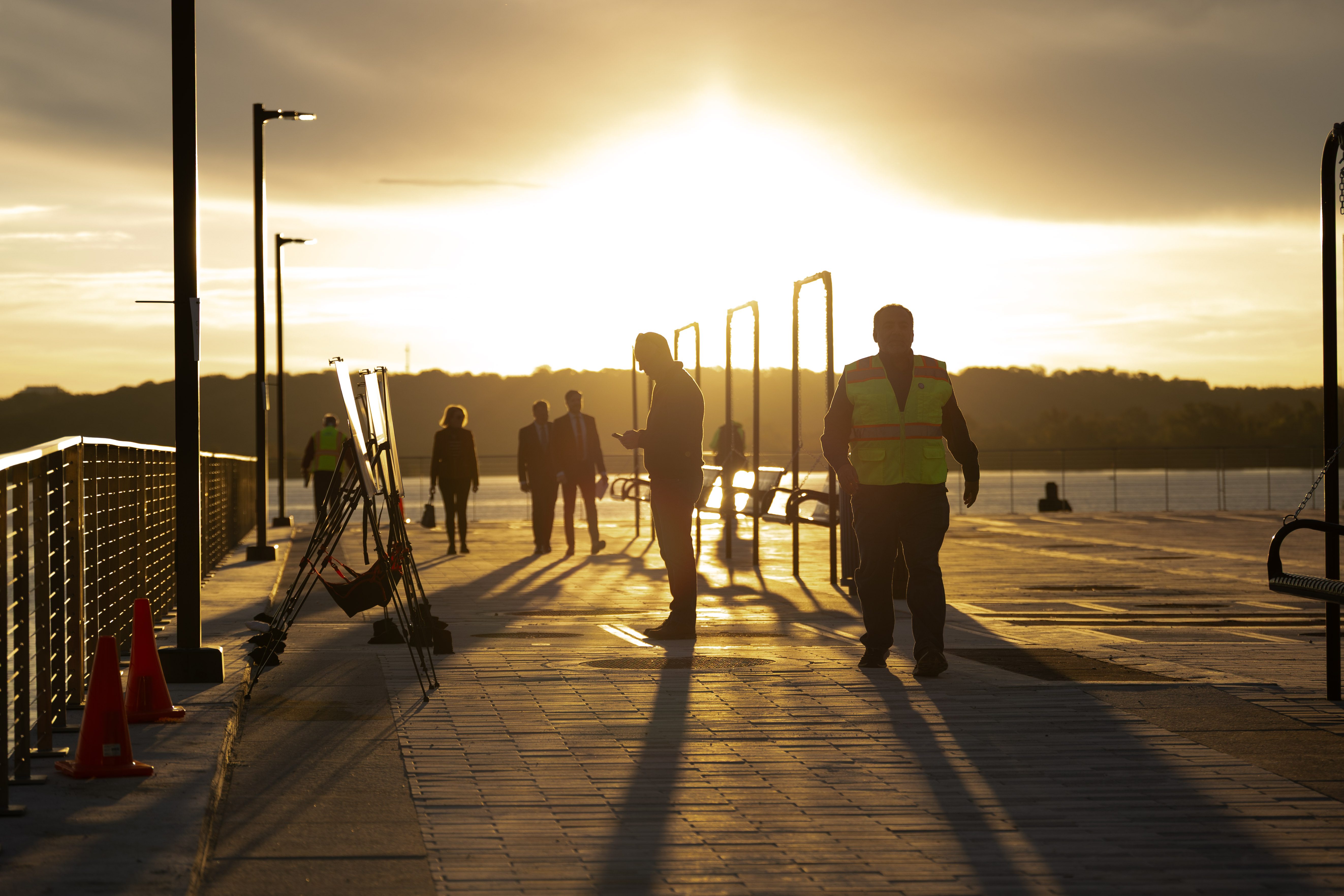 People silhouetted by the rising sun look at informational signs.