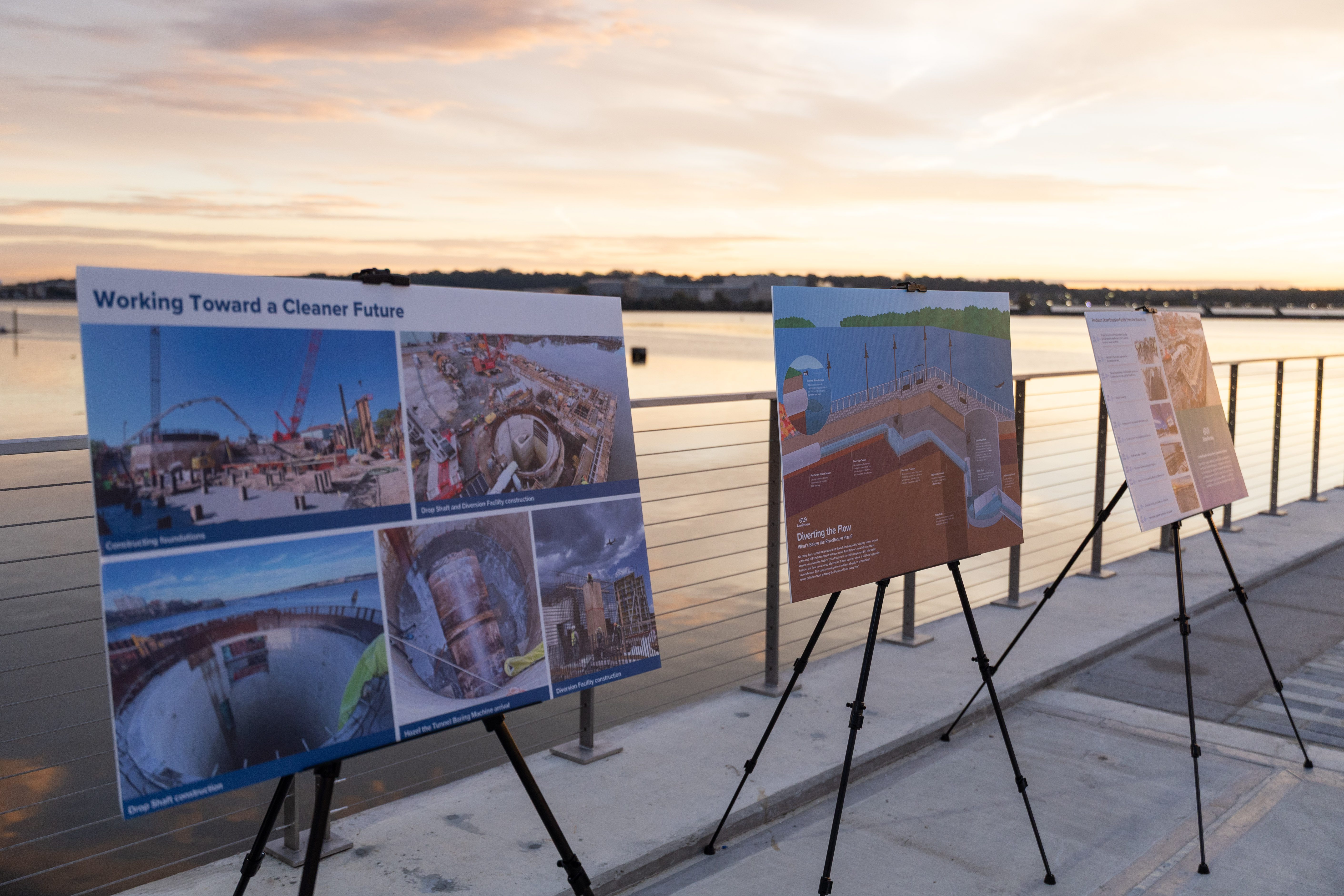 Informational signs describe the construction process. The sunrise reflects off the river in the background.