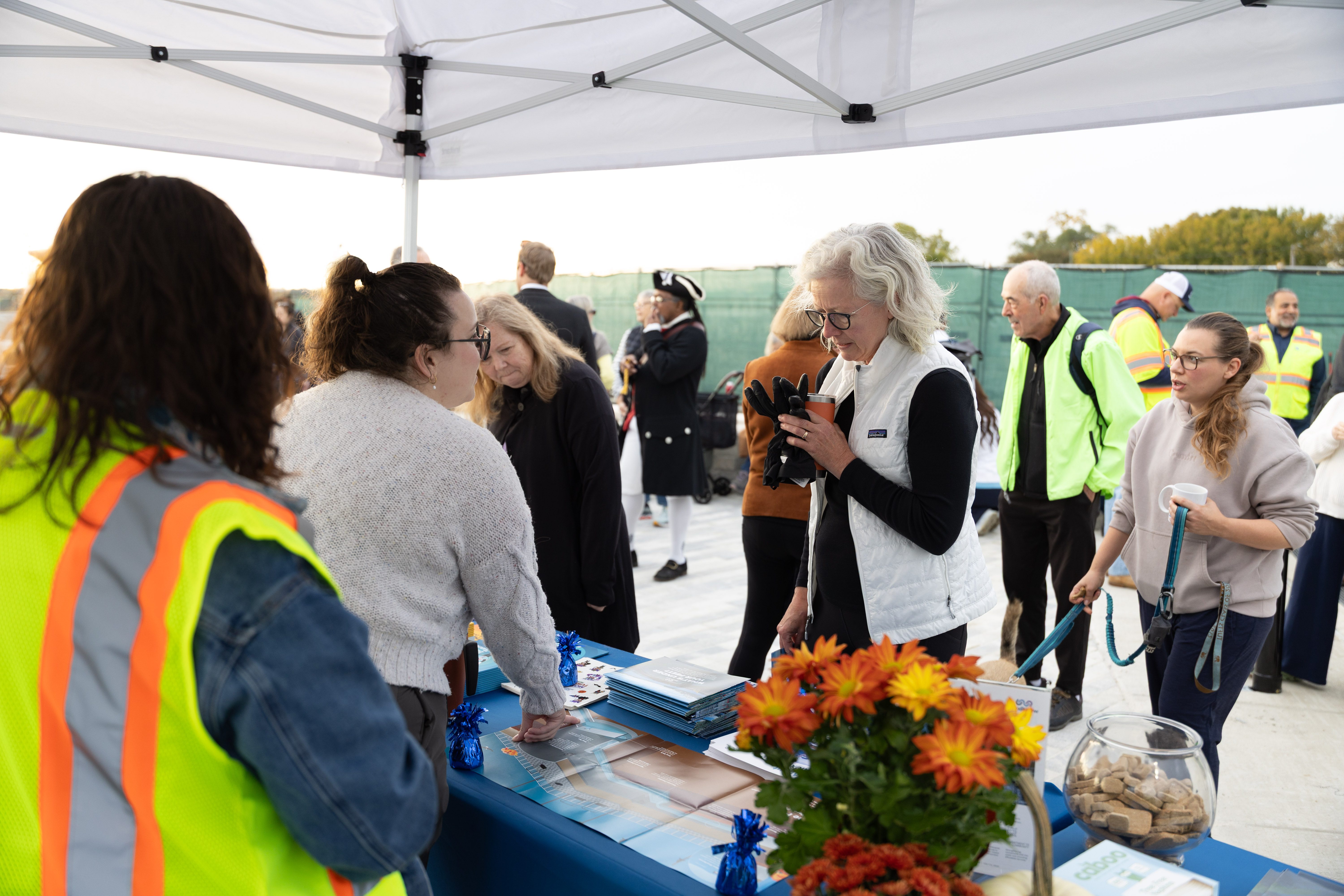 Members of the public talk to AlexRenew employees standing behind an informational table with orange flowers decorating it.