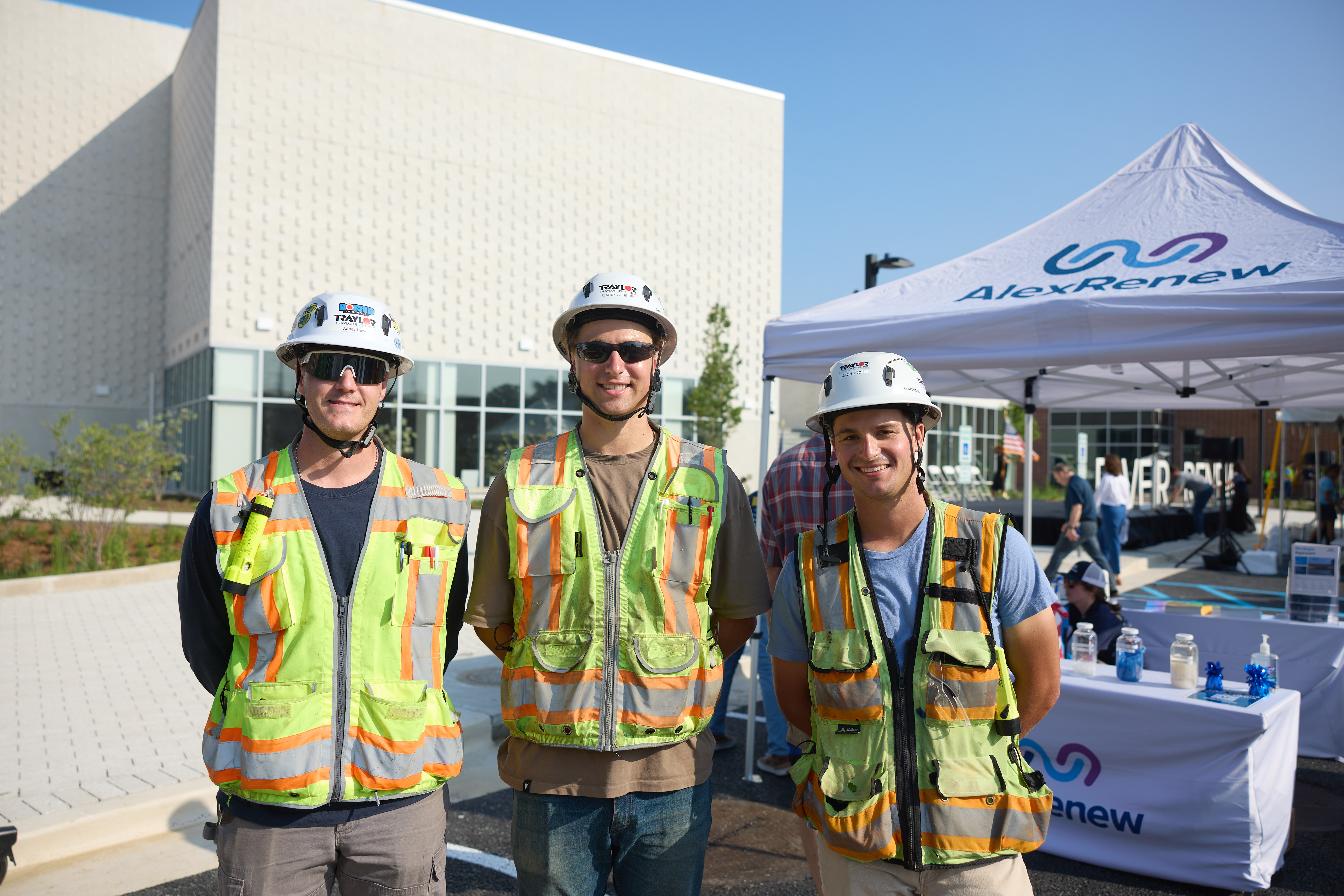 three people in high visibility safety gear and helmets smile at the camera