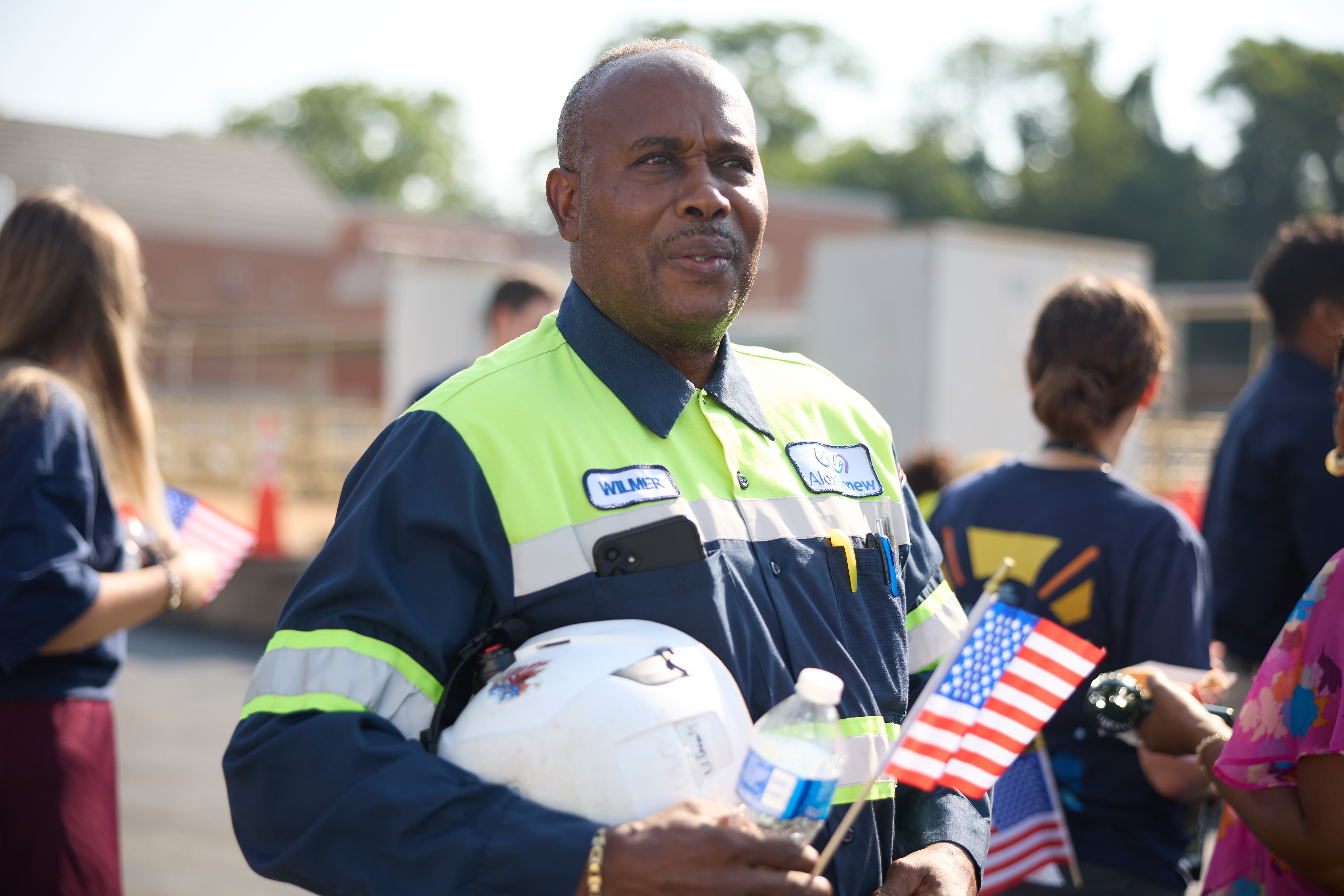 A man wearing a high vis uniform holds an American flag and looks off into the distance