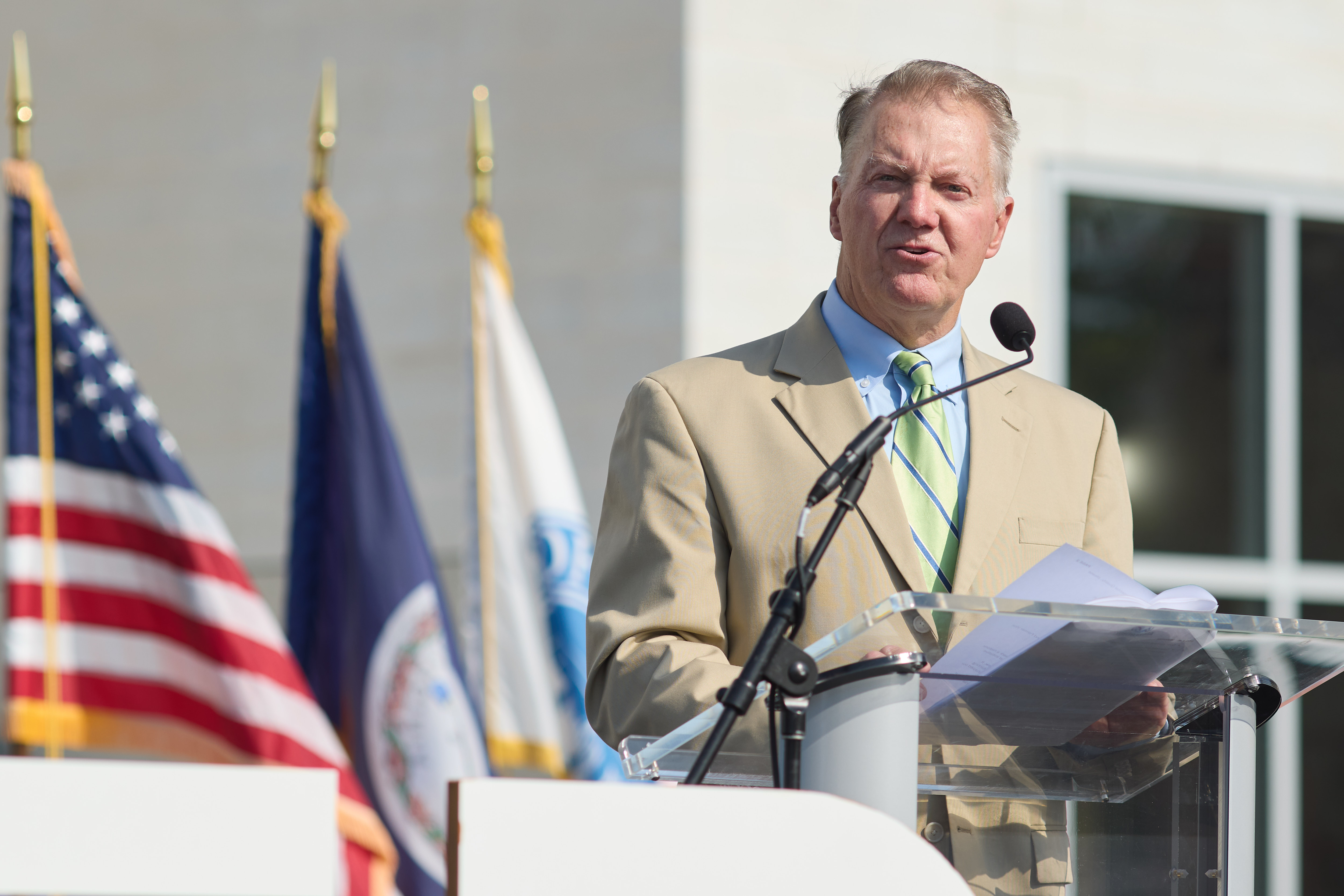 a man in a suit at the podium with flags in the background