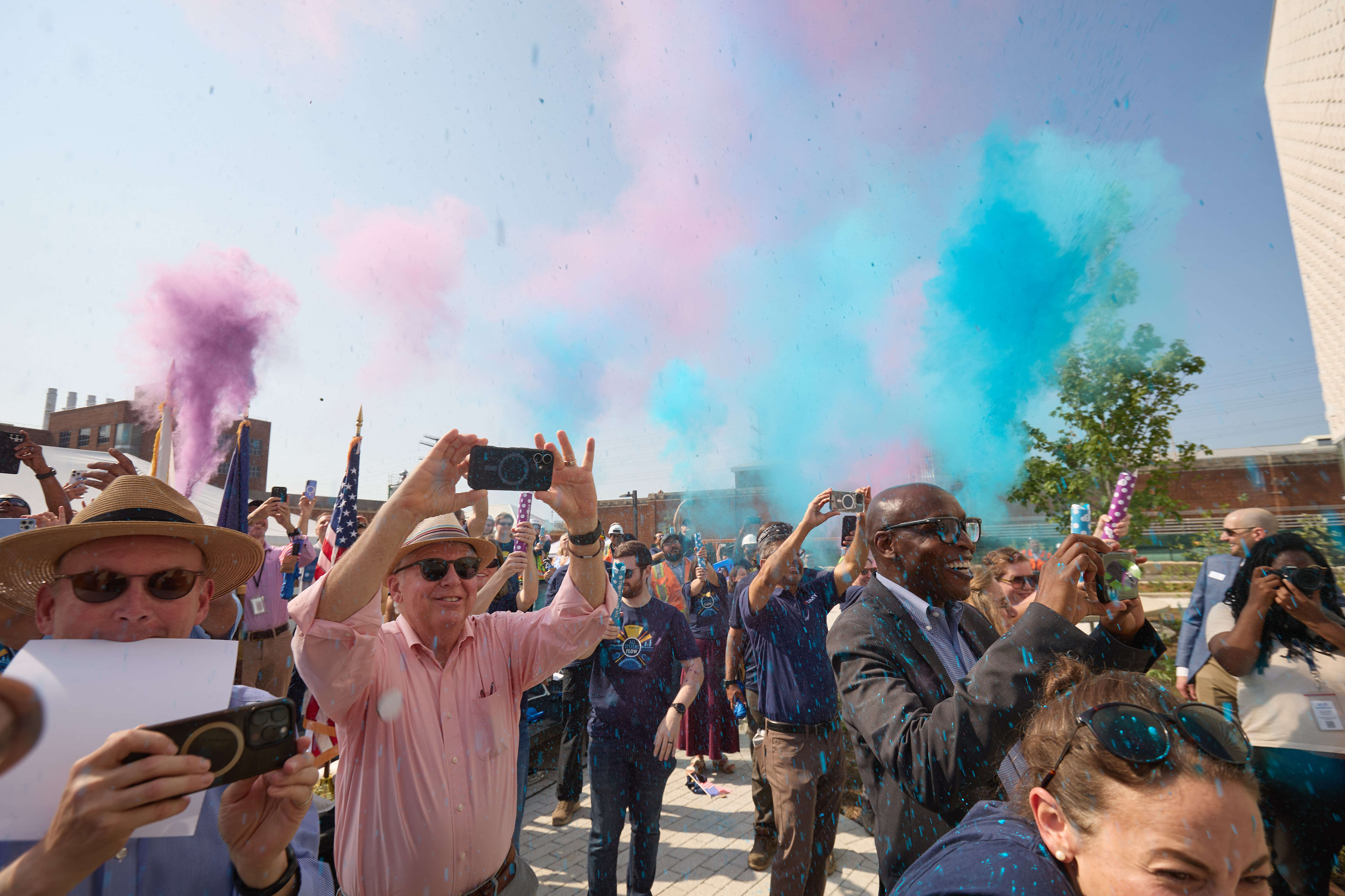 People cheer as colored smoke rises in the air after a ribbon cutting.