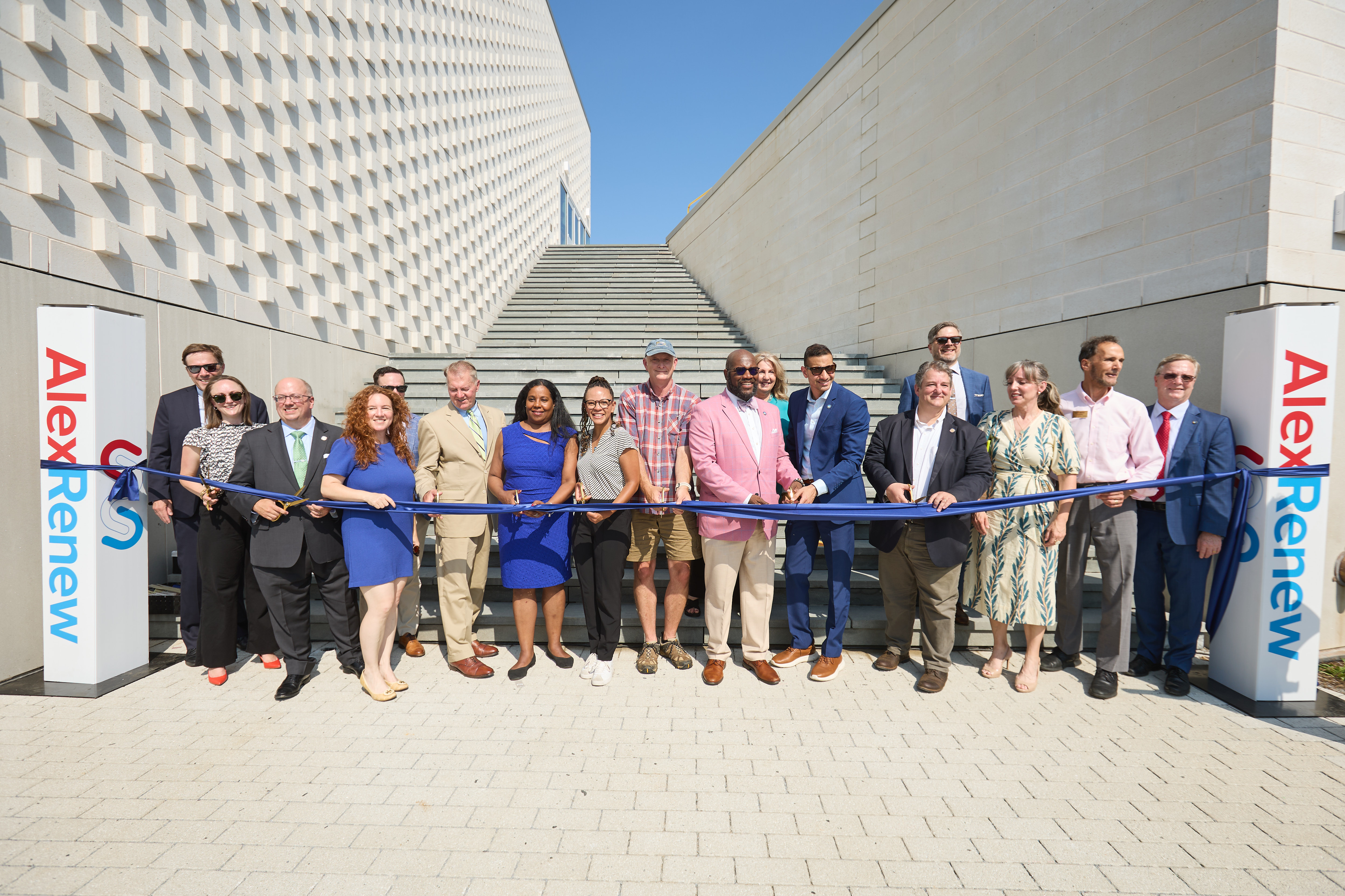 Several people pose before a ribbon in front of a white building.