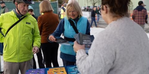 An elderly couple examine pamphlets at an AlexRenew informational table. An AlexRenew employee on the right side of the frame offers assistance.