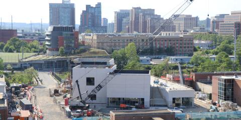 A photo of the pumping station superstructure, a white building under construction. In the background is a skyline of apartment buildings and AlexRenew's office.